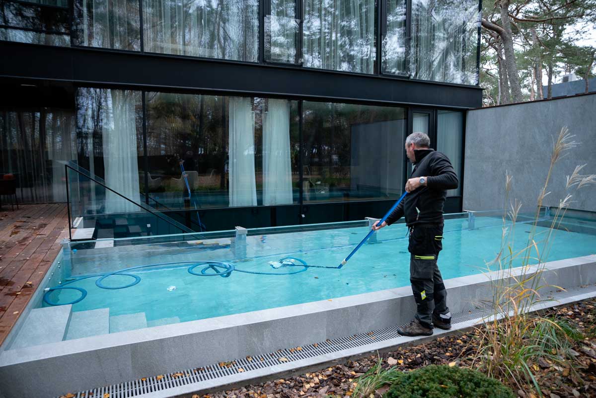 Piscină în aer liber cu apă tulbure și murdară, pete maronii și murdărie vizibile la suprafață, o persoană stând lângă piscină