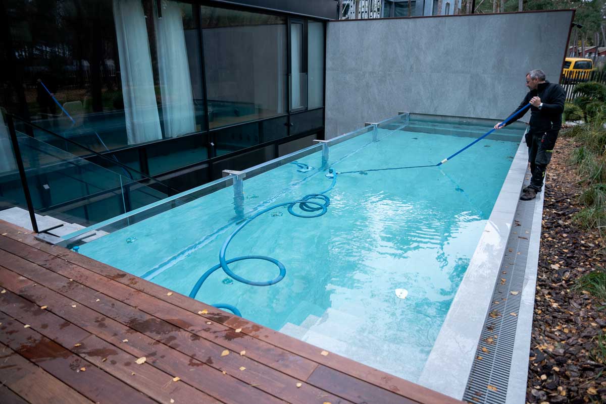 O piscină cu apă verde deschis și tulbure, suprafața acoperită cu un strat de alge, o situație surprinsă în care o persoană curăță piscina.
